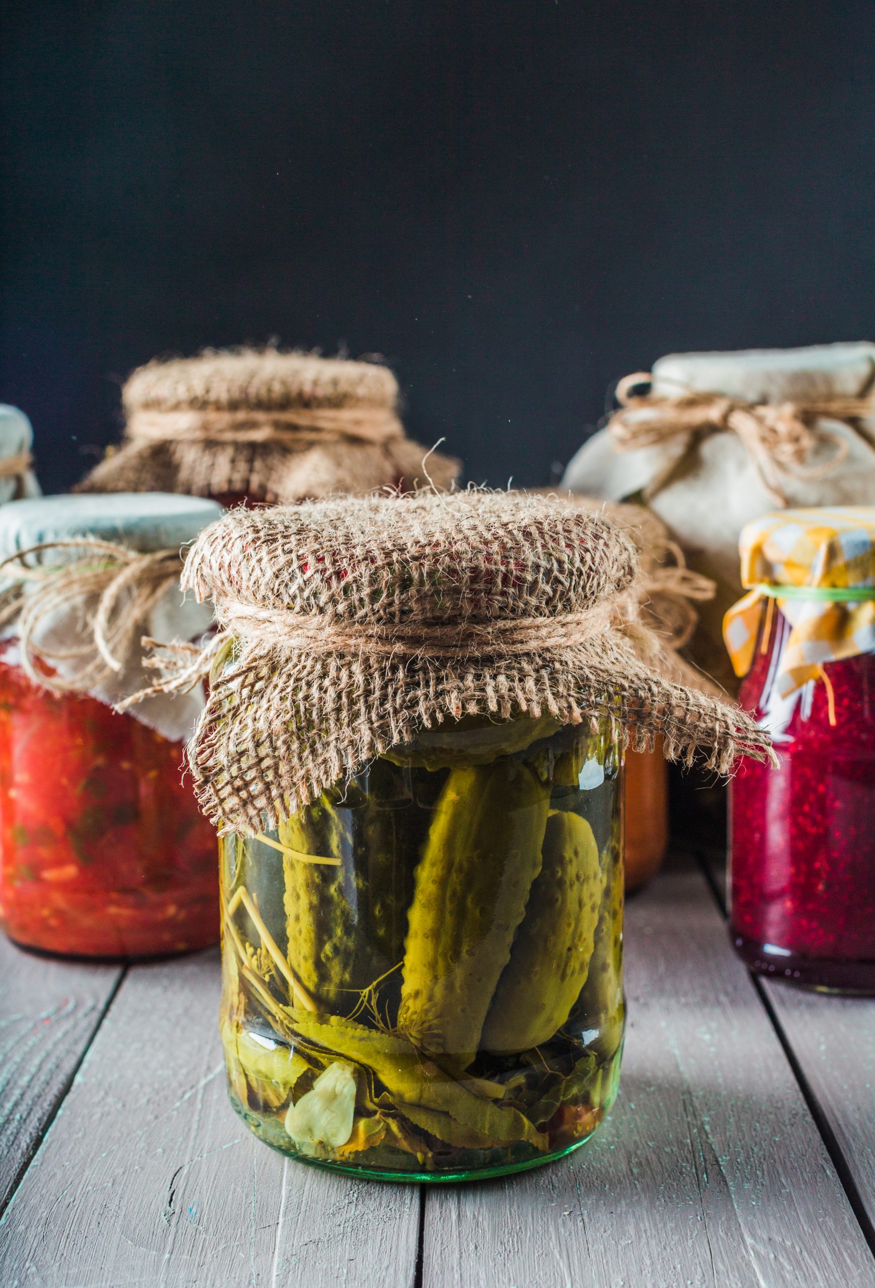Several jars filled with pickles and colorful preserves sit on a wooden surface.