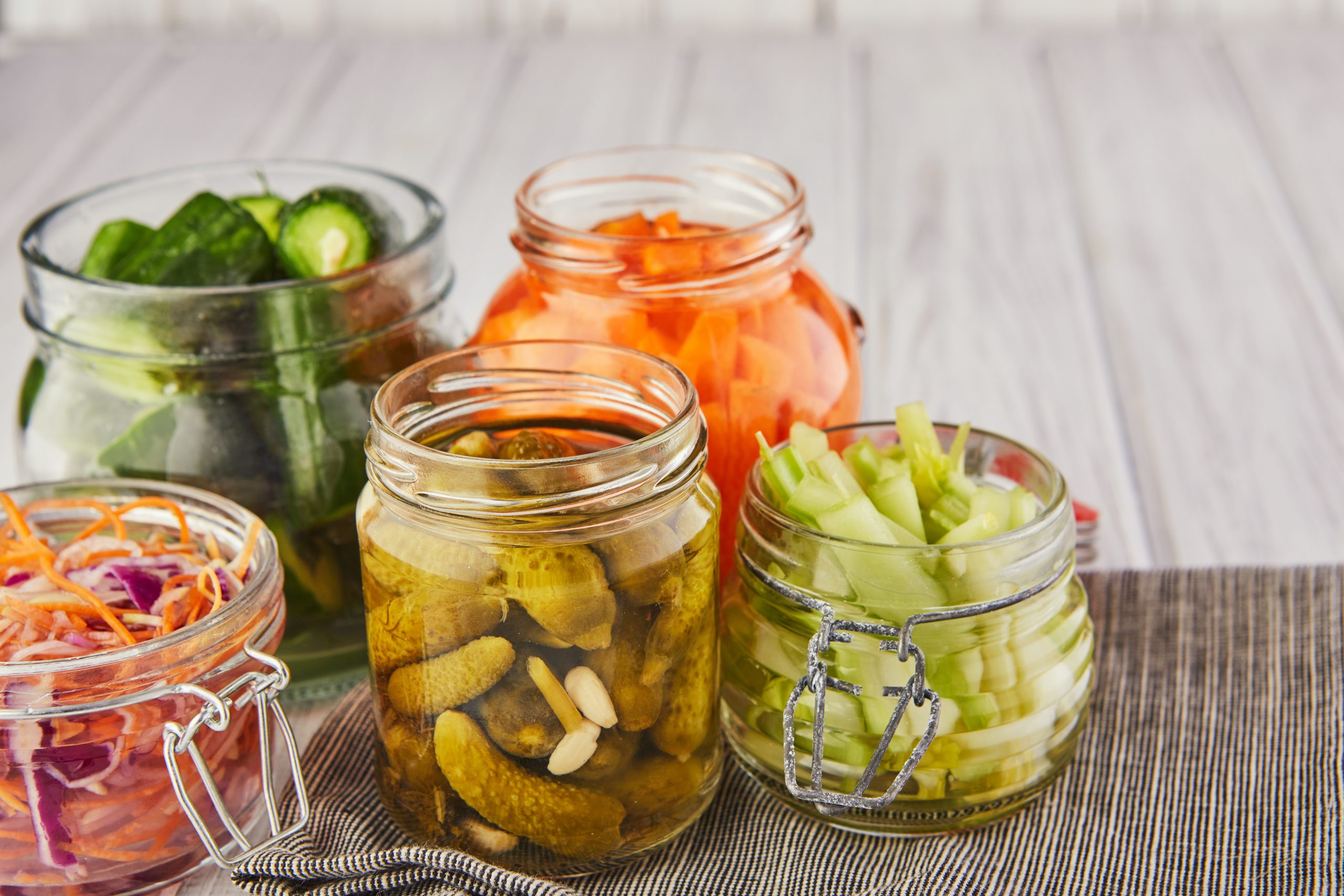 Fermented preserved vegetarian food concept. Sour sauerkraut, pickled carrots, pickled cucumbers, pickled celery in glass jars on a white wooden kitchen table. The concept of canned food. Copy space