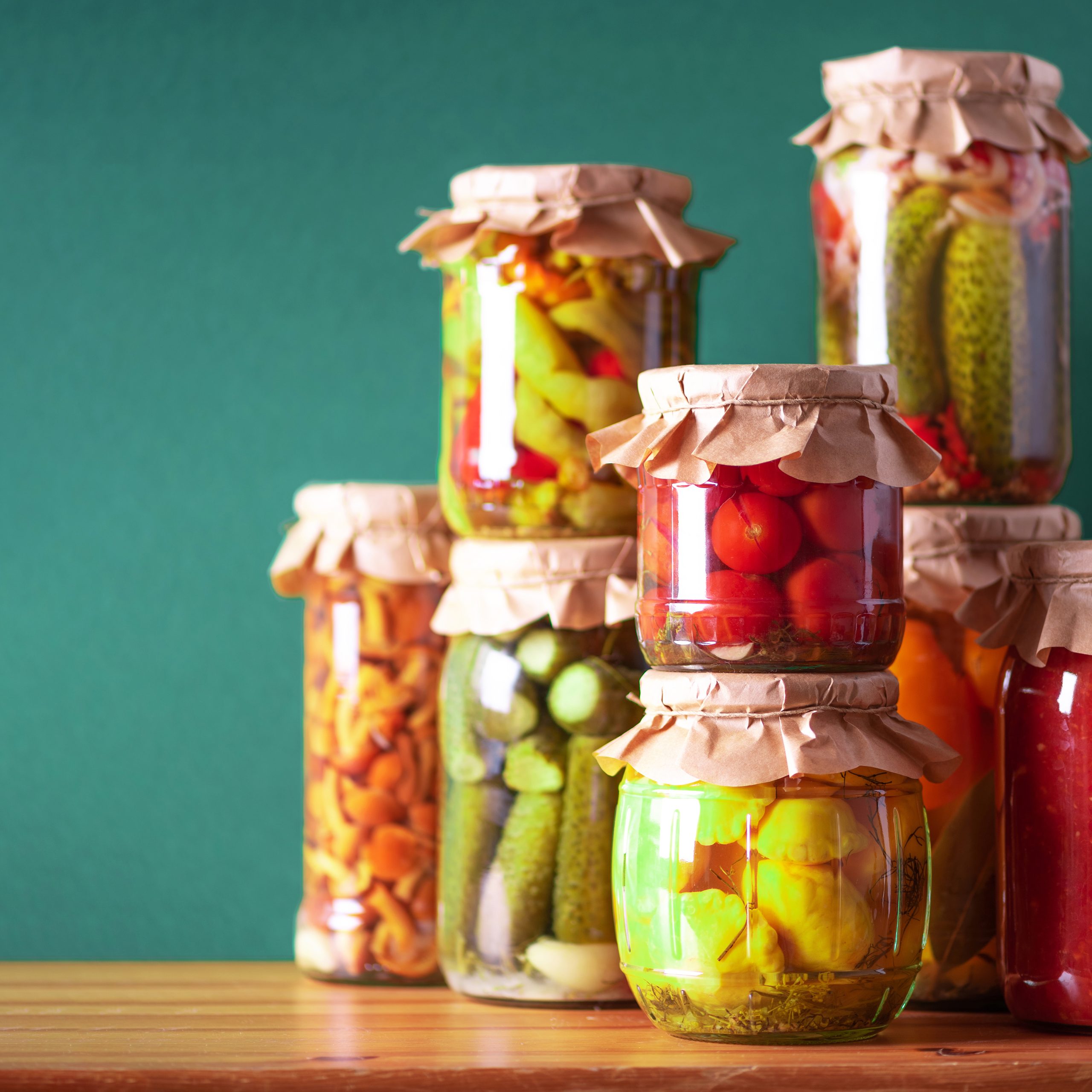 Preserved vegetables in glass jars on green background. Copy space. Healthy fermented food concept. Harvest concept.